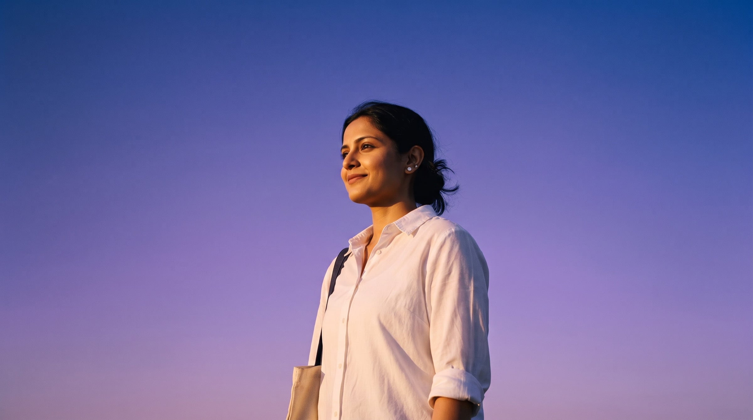 A woman in a white shirt smiles toward the evening light against a violet sky.